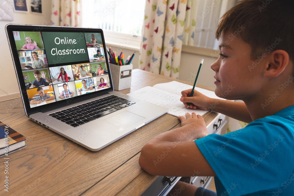 Caucasian boy using laptop for video call, with waving diverse elementary school pupils on screen