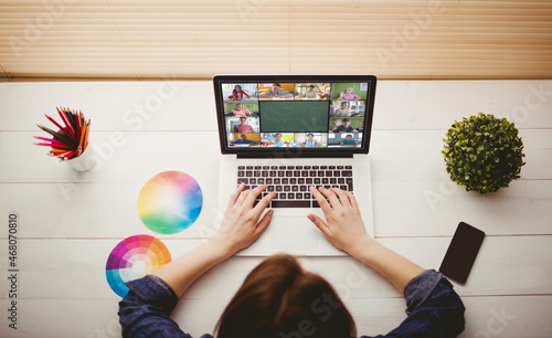 Caucasian woman using laptop for video call, with smiling diverse elementary school pupils on screen