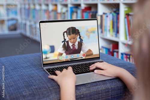 Caucasian girl using laptop for video call, with elementary school pupil on screen