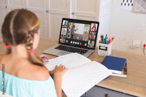 Caucasian girl using laptop for video call, with smiling diverse elementary school pupils on screen