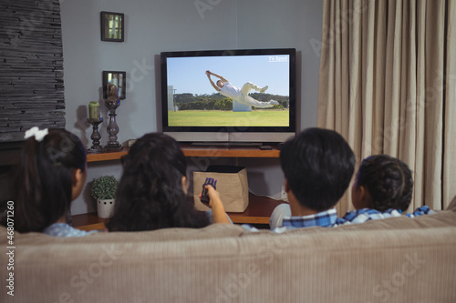 Rear view of family sitting at home together watching sports event on tv