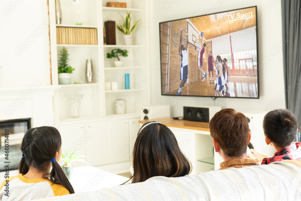 Rear view of family sitting at home together watching basketball match on tv Rear view of family sitting at home together watching basketball match on tv