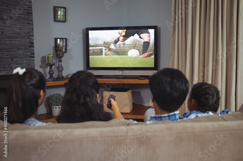 Rear view of family sitting at home together watching football match on tv