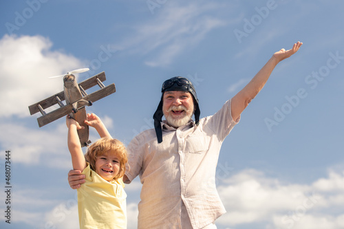 Young grandson and old grandfather with toy jetpack plane against sky. Child pilot aviator with plane dreams of traveling.