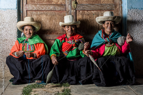 Mujeres andinas latinoamericanas, sentadas, tejiendo lana y sonriendo felices