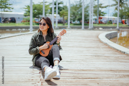 Playing Ukulele of Young Beautiful Asian Woman Wearing Jacket And Black Jeans Posing Outdoors © Sino Images Studio