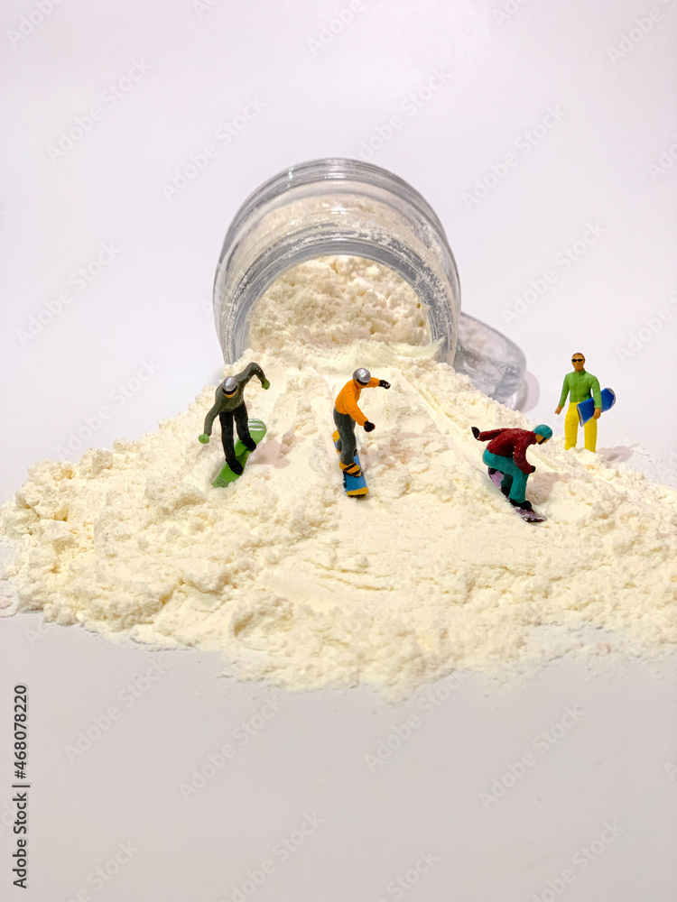 Miniature snowboard lovers are playing with flour spilling from a bottle.  They are racing to become champions. Stock Photo | Adobe Stock