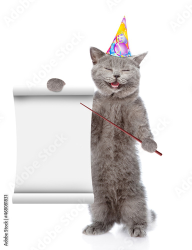 Happy cat wearing birthday cap points on empty list. isolated on white background