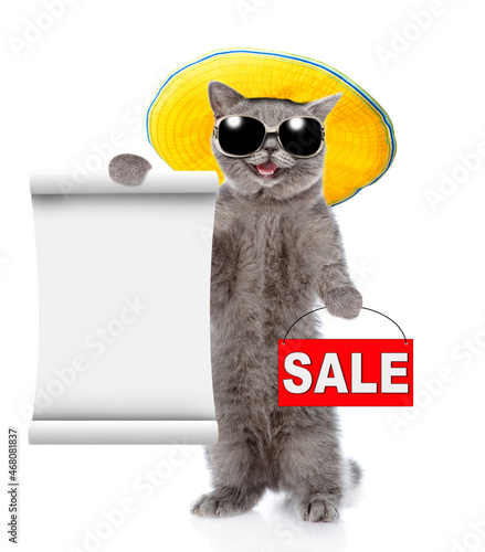 Happy cat wearing sunglasses and tiny summer hat holds sales symbol and shows empty list. isolated on white background