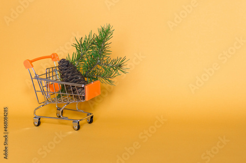 Christmas cart with a Christmas tree branch on a yellow background. Concept for Christmas shopping, sale. Festive trolley