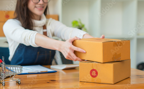 Young Asian woman entrepreneur working at home office, BOX,smartphone,laptop, online, marketing, packaging, delivery, SME, e-commerce concept.