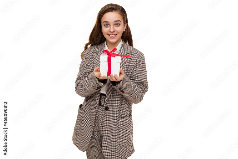 Photo of beautiful cute pretty happy smiling brunette teenage girl with long hair in stylish plaid jacket, plaid pants and white shirt holds white box with red ribbon with a gift isolated on white Photo of beautiful cute pretty happy smiling brunette teenage girl with long hair in stylish plaid jacket, plaid pants and white shirt holds white box with red ribbon with a gift isolated on white