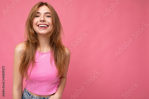 Emotional happy young charming dark blonde woman with sincere emotions isolated on background wall with copy space wearing stylish pink top. Positive concept
