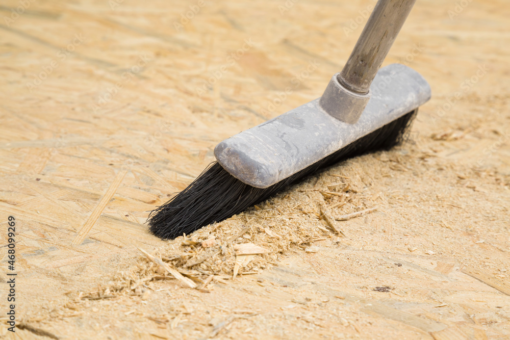 Broom sweeping sawdust from osb board floor. Cleaning garbage after