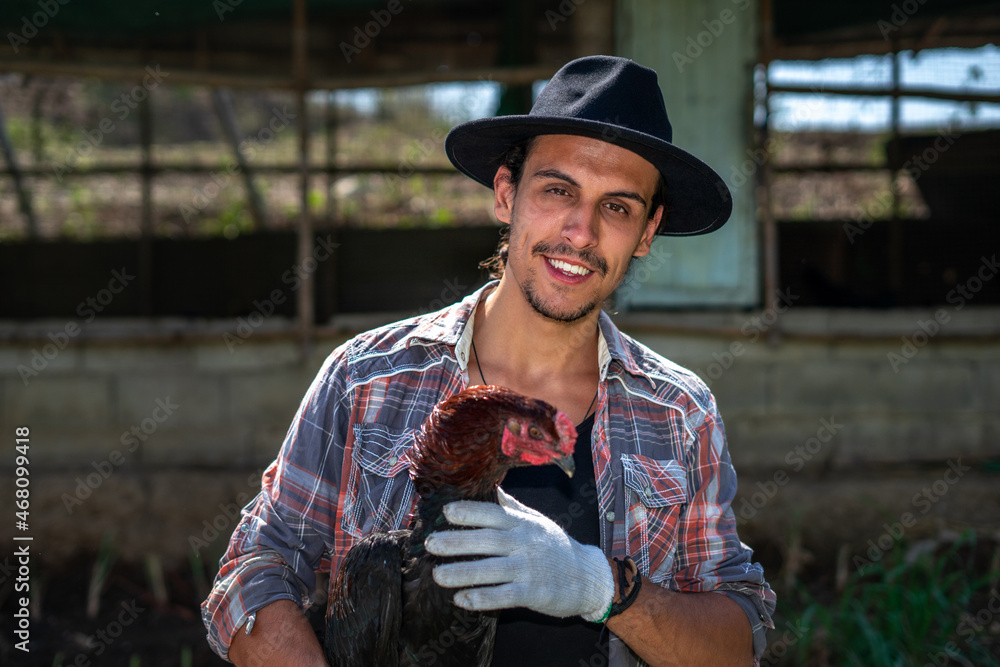 Close-up of Portrait of a cheerful farmer holding and taking care of chicken outdoor. A smart hipster young man holding a hen has been satisfied smiling at an organic sustainable egg farm