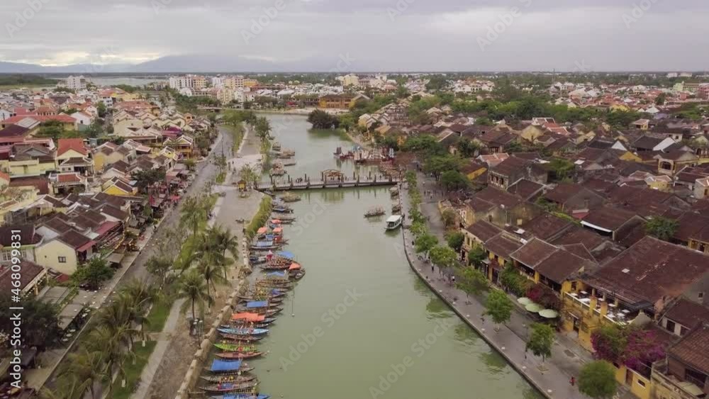 Hoi An river and urban landscape. Wide transport channel with green water bridge and colorful moored boats in historical large city aerial view Hoi An river and urban landscape. Wide transport channel with green water bridge and colorful moored boats in historical large city aerial view