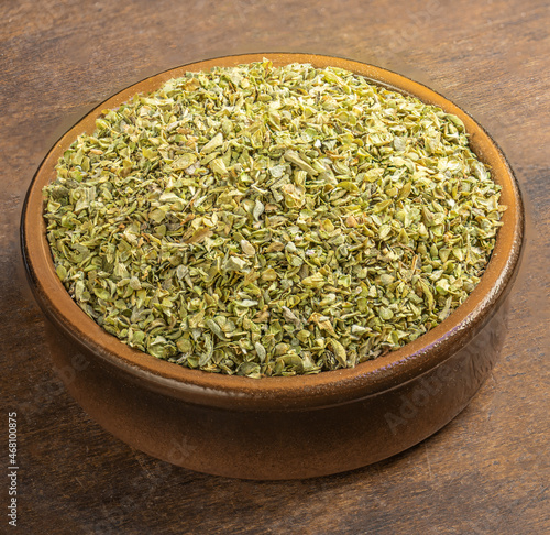 Dried oregano spice on a wooden background. Heap of oregano in a clay bowl.