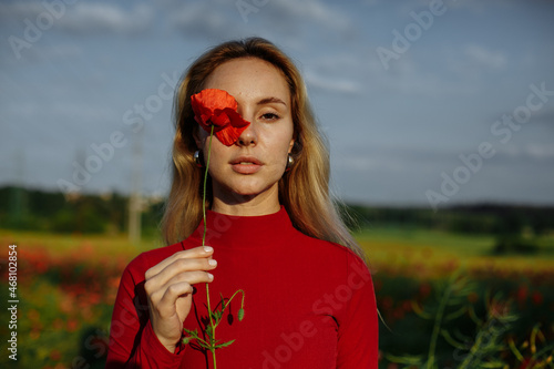 girl in a red sweater in a field with red poppies holding a red poppy in her hand