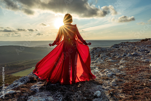 Rise of the mystic. sunset over the clouds with a girl in a long red dress. Stands on the mountain with a magical view.