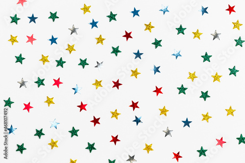 White background with colored sequins in the shape of stars. Festive backdrop for your projects. Background for your product presentation. Christmas texture. Top view, copy space.