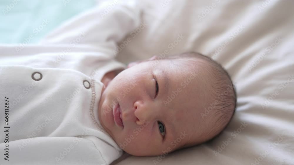 Close up newborn baby in white clothes. Baby in a light blouse wakes up and grimaces. Close up newborn baby in white clothes. Baby in a light blouse wakes up and grimaces.