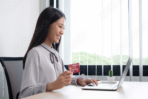 The Asian businesswoman's hand is holding a credit card and using a laptop for online shopping and internet payment in the office