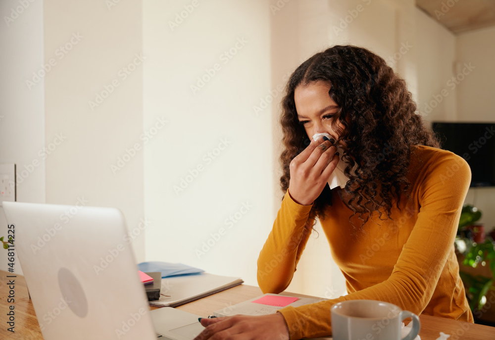 Multi-cultural young adult female blowing her nose while working from home on her laptop. Modern apartment Multi-cultural young adult female blowing her nose while working from home on her laptop. Modern apartment