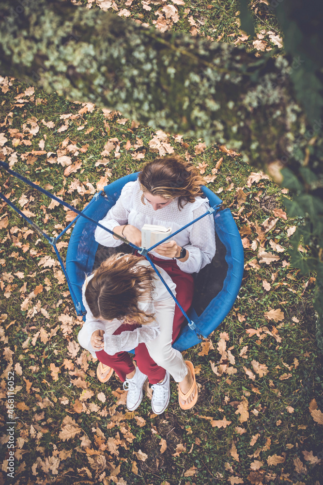 Fototapeta premium two sisters reading a book in a swing in autumn