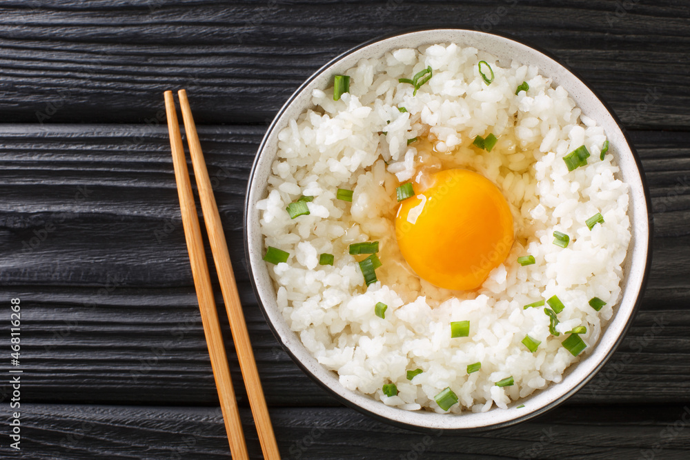 Tamago kake gohan is a simple Japanese dish made of raw Egg Over Rice close up in the bowl on the table. Horizontal top view from above Tamago kake gohan is a simple Japanese dish made of raw Egg Over Rice close up in the bowl on the table. Horizontal top view from above