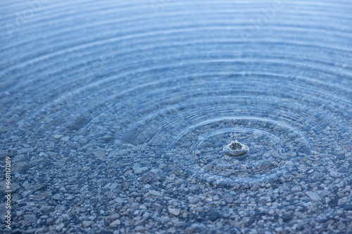 Wassertropfen erzeugen Wellen in einem See mit Steinen am Grund. Das Bild wirkt sehr beruhigend und aufgeräumt.