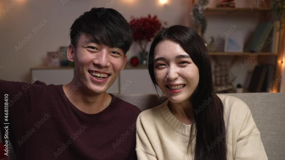 Happy young couple sit on couch in living room look at camera talking on video call at home at night. smiling millennial man and woman having webcam conversation using unlimited internet connection Happy young couple sit on couch in living room look at camera talking on video call at home at night. smiling millennial man and woman having webcam conversation using unlimited internet connection