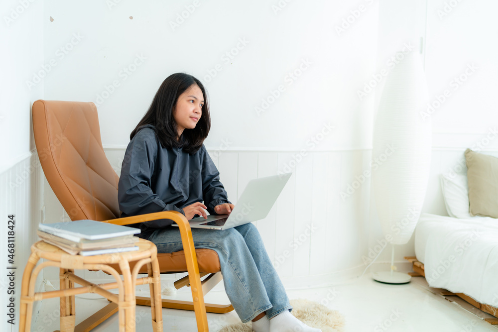 Portrait, a cute Asian teenage girl. wearing gray shirt studying online with notebook computer in bed in the bedroom with a thinking face Portrait, a cute Asian teenage girl. wearing gray shirt studying online with notebook computer in bed in the bedroom with a thinking face
