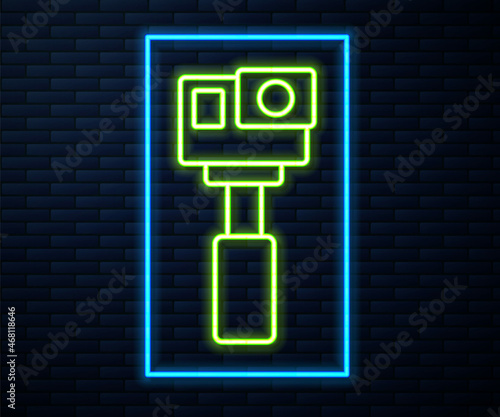 Glowing neon line Action extreme camera icon isolated on brick wall background. Video camera equipment for filming extreme sports. Vector