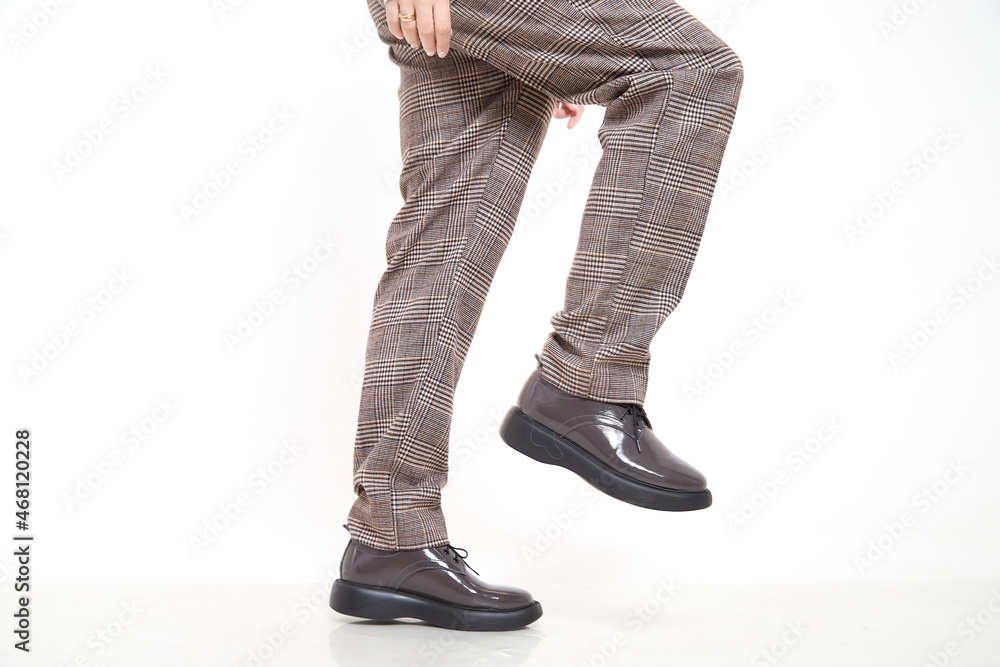 Fototapeta premium Brown female or male patent leather shoes on legs of woman. Shooting for a catalog or an online store. A pair of shoes