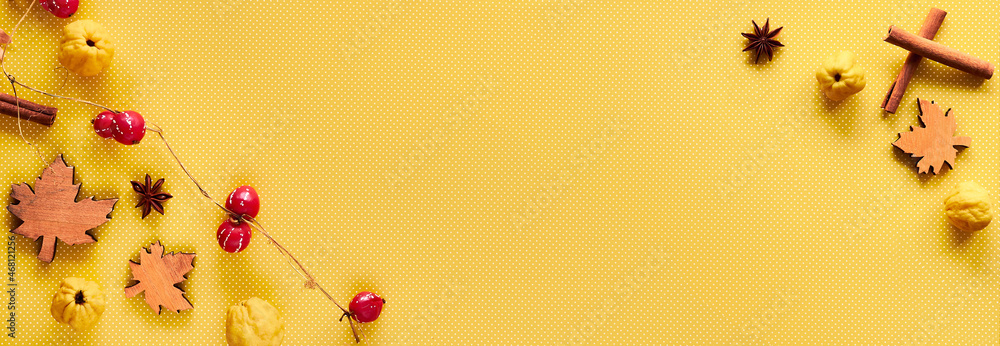 Fototapeta premium Autumn decorations on yellow paper with copy-space. Quince fruits, natural garland, wooden deco leaves, anise spaces. Panoramic banner composition on yellow paper.