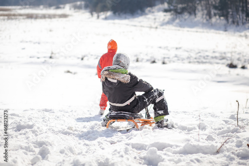 A boy in a ski suit on a snow mountain with a sled. The child is riding a sledge scooter . Active games on the street. Healthy lifestyle