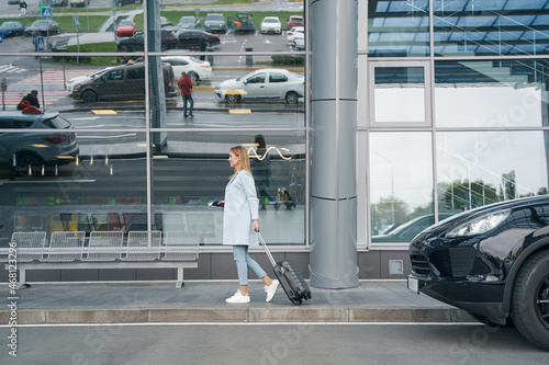 Smiling happy tourist wheeling her trolley suitcase outdoors