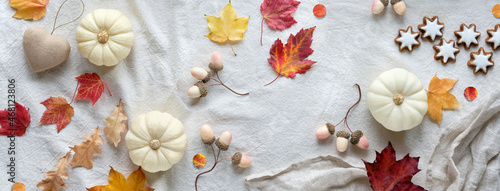 Off white natural Fall decorations with copy-space. Flat lay on white textile, place for text. Pumpkins, dry leaves and rowan berries, star cookies, dry leaves and craft cardboard heart.