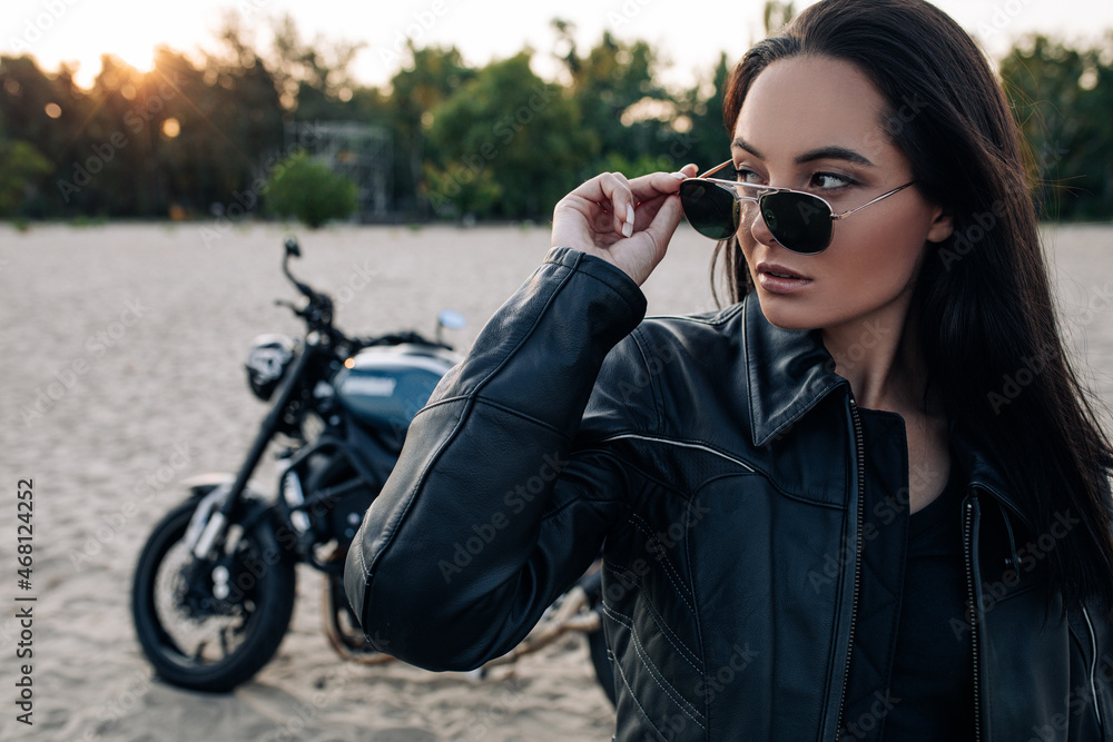 Young woman stands near black motorbike on beach at sunset. Young woman stands near black motorbike on beach at sunset.
