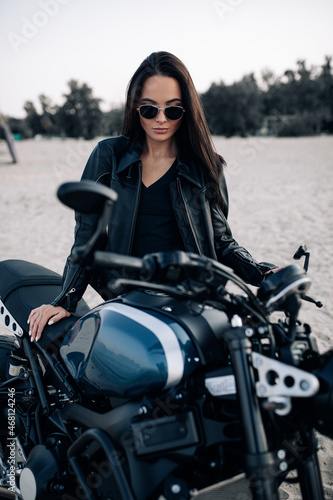 Young woman stands near black motorbike among sandy beach. © Stanislav