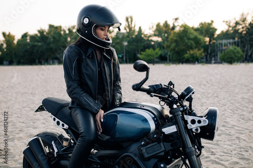 Young woman sits on black motorbike in helmet on beach. © Stanislav
