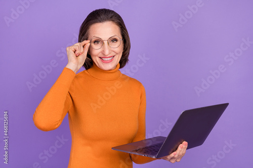 Photo of smart clever retired woman wear orange pullover arm spectacles working modern gadget isolated violet color background © deagreez