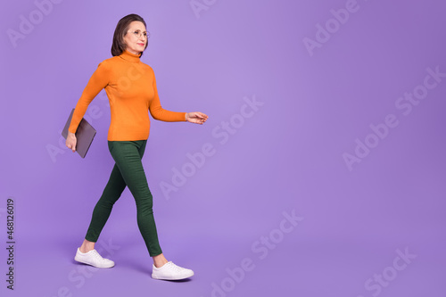Photo of clever confident lady dressed orange turtleneck glasses holding modern device walking empty space isolated purple color background