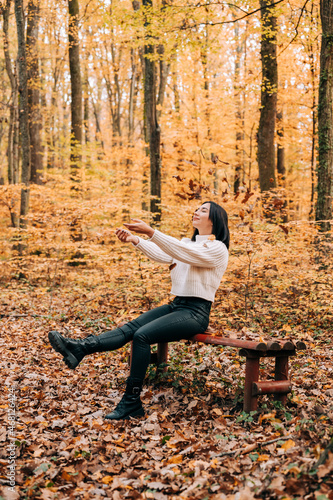 Cute girl smiling, jumping and playing with the leaves in the woods during the autumn season.