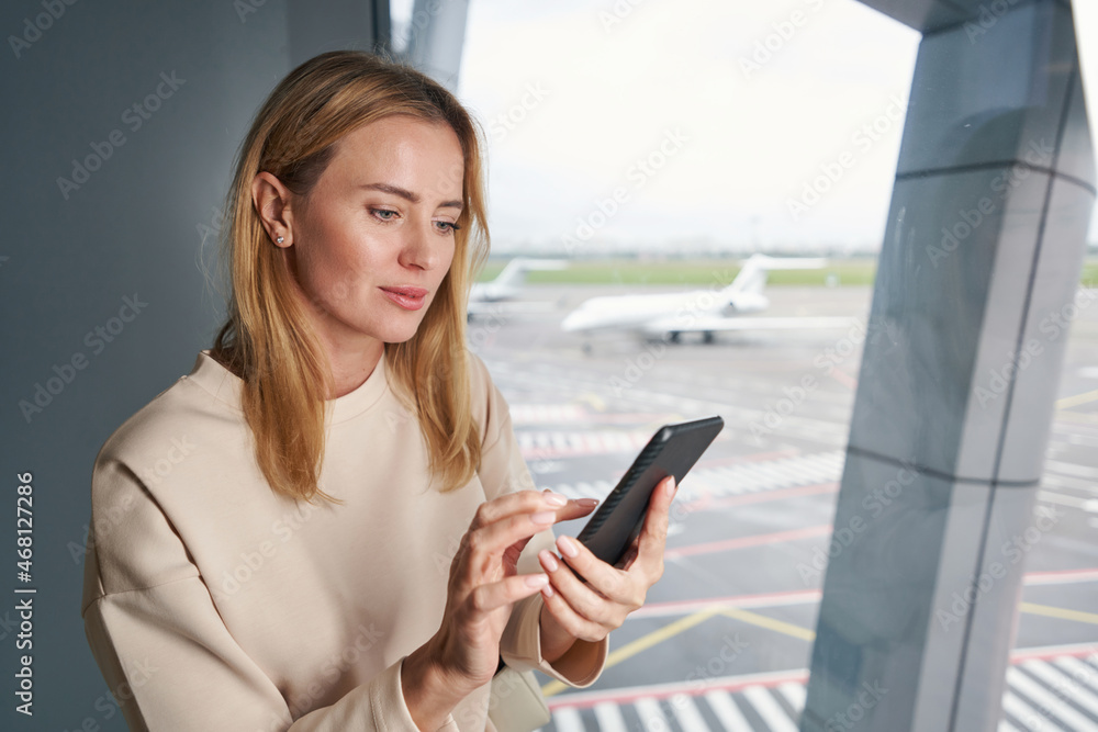 Focused Caucasian young traveler using her cellphone indoors