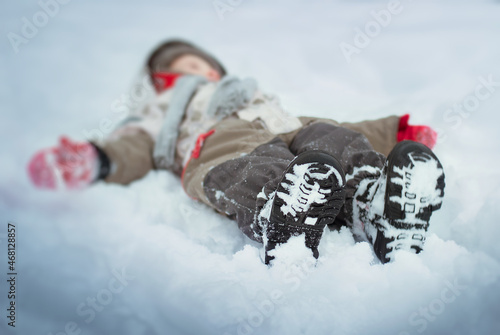 a child in winter clothes licks in the snow, the face is not visible, the sole of winter boots is clearly visible, the protector