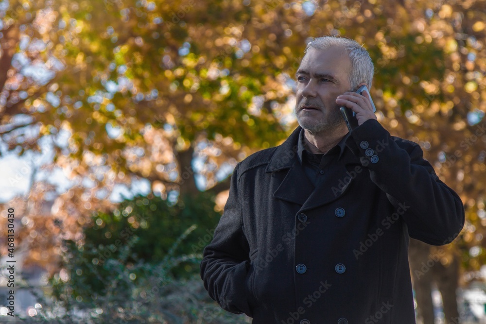 man in coat using his mobile phone on autumn background man in coat using his mobile phone on autumn background