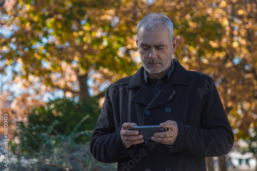 man in coat using his mobile phone on autumn background