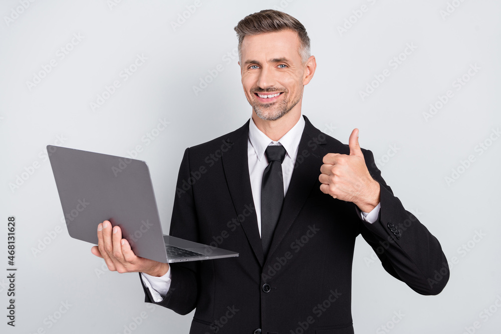 Photo of confident happy young programmer wear black jacket showing thumb up developing modern device isolated grey color background Photo of confident happy young programmer wear black jacket showing thumb up developing modern device isolated grey color background