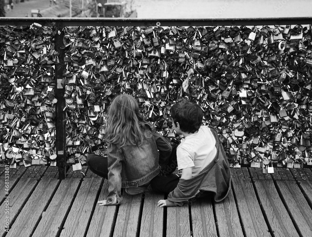 Boy and girl (unrecognizable, back view) playing at Love locks bridge in Paris, France. Valetines day concept. Romantic travel background. Black white historic photo
